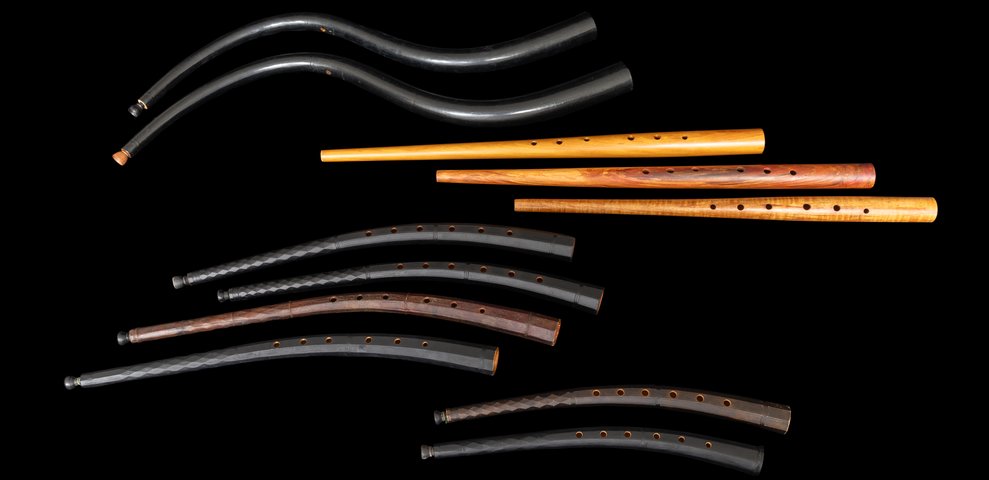 Collection of historic zinks and cornets in various sizes against black background.