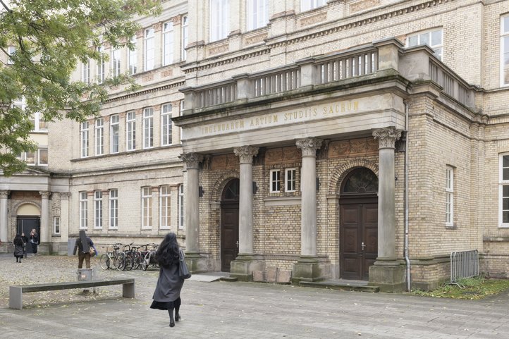 Historic building at Dechanatstraße housing the Faculty of Music, University of the Arts Bremen, featuring classical architecture with columns and large windows. Students are gathered outside, and bicycles are parked nearby.