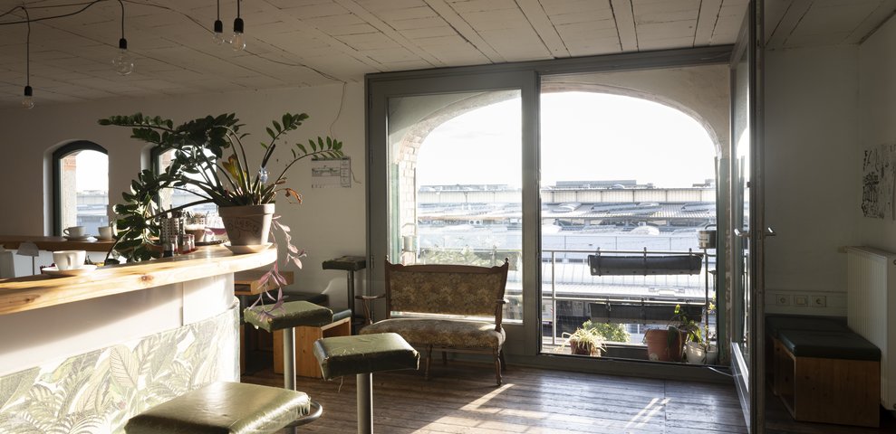Sonnenlicht durchflutet den Raum des Café Lu der HfK Bremen, Pflanzen und Möbel im Vordergrund.