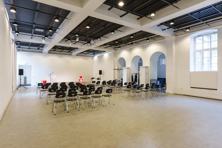 Bright gallery at HfK Bremen with rows of empty chairs, a microphone stand, and modern lighting system.