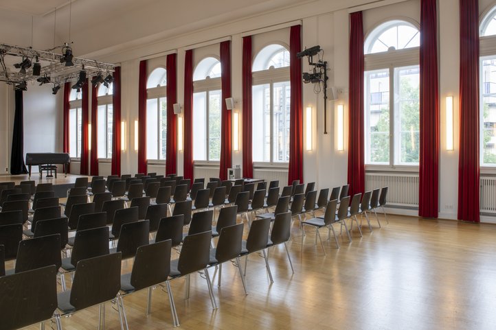 Konzertsaal der HfK Bremen, leere Stühle, Bühne mit rotem Vorhang.