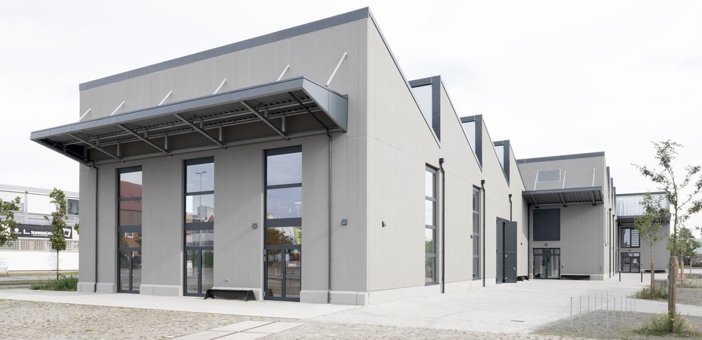 Speicher XI A at HfK Bremen, showcasing modern architectural design with large windows and a minimalist facade, set in a cobblestone courtyard.