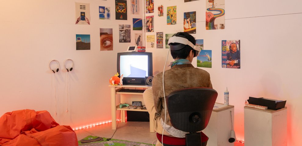 Interactive installation with VR headset and cathode ray monitor in room decorated with posters.