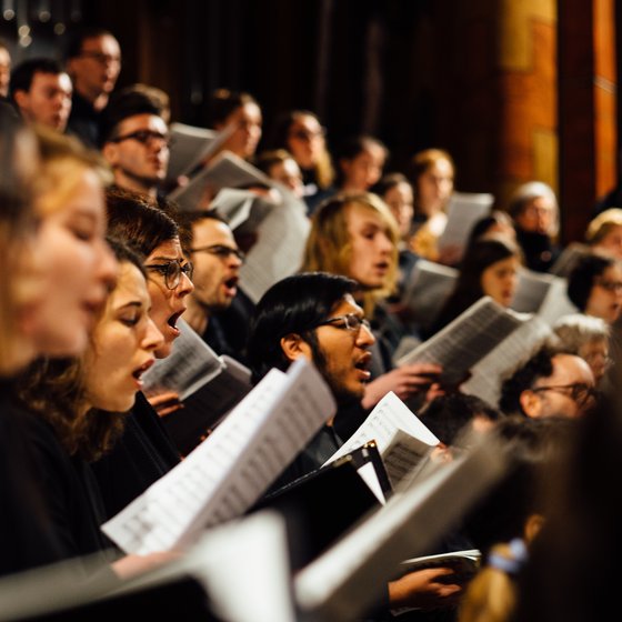 Choir singing in unison, holding sheet music in a dimly lit church.