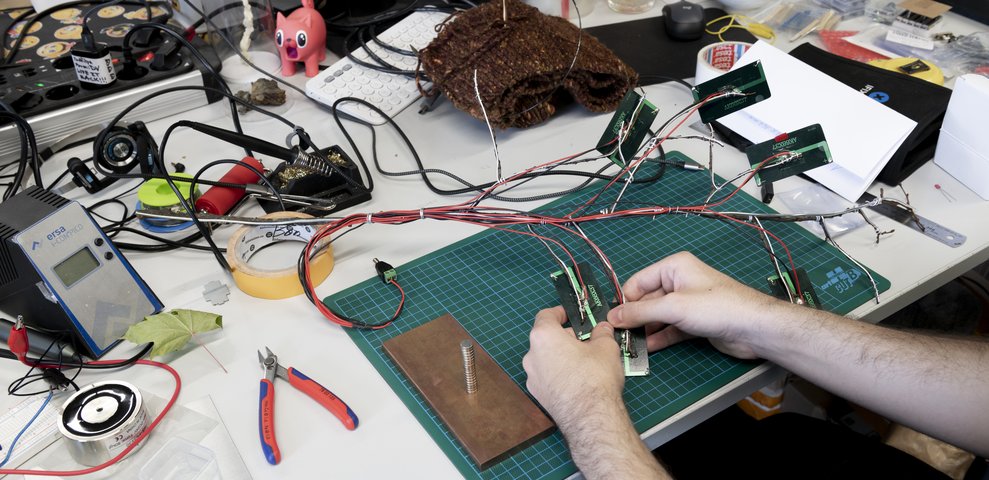 Close-up of soldering and electronics work on cutting mat in project space.