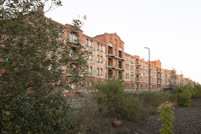 Historic red-brick exterior of Speicher XI at HfK Bremen, featuring uniform windows and foliage in the foreground.