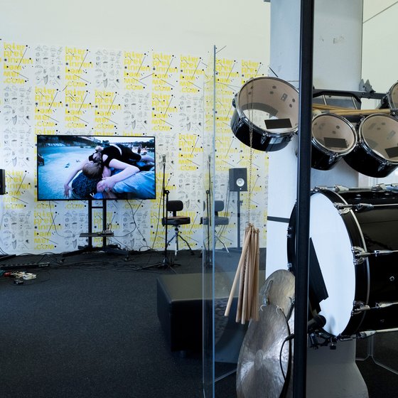 Music studio with instruments, a TV showing a performance, and walls covered in artistic posters.
